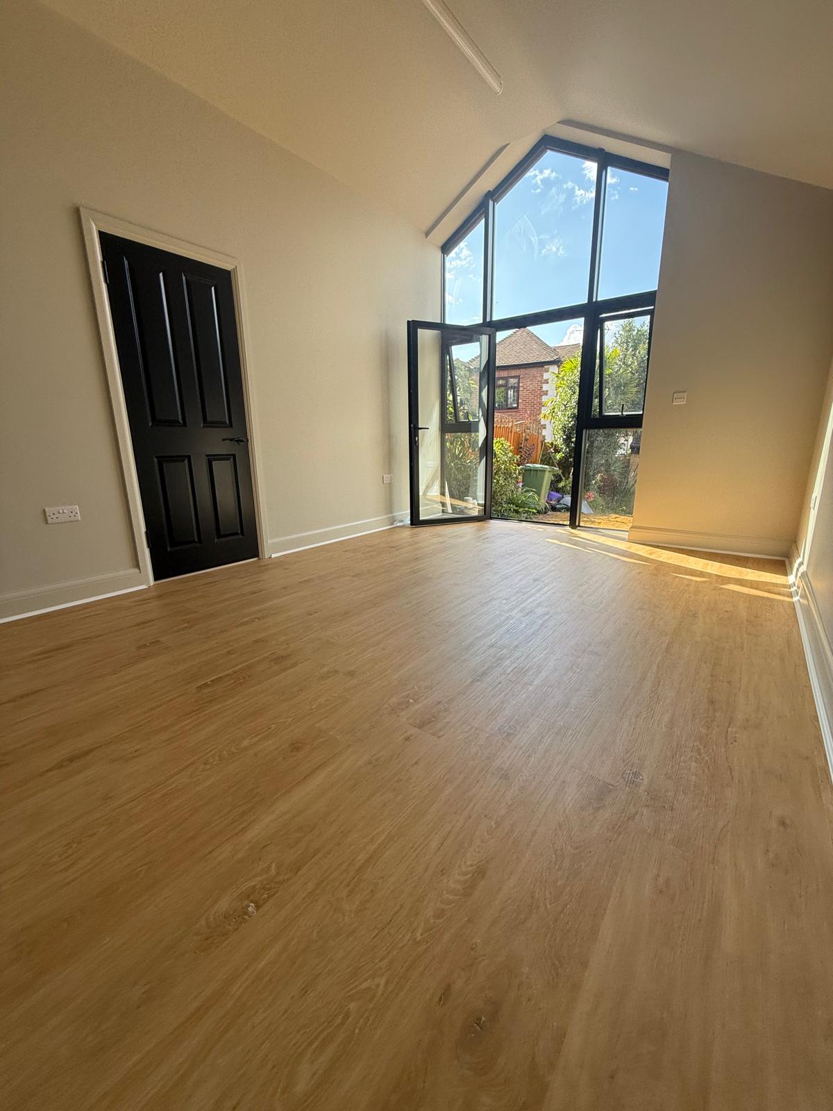 Natural oak plank floor in a vaulted garden room with full-height black framed gable glazing