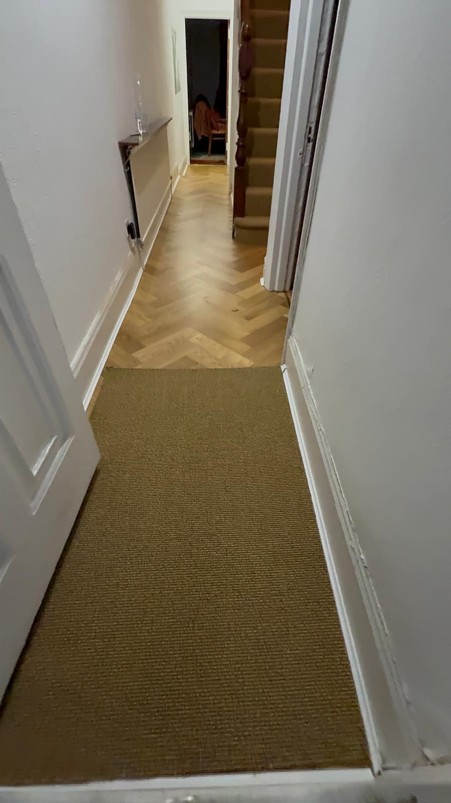 Natural woven carpet in a hallway meeting an oak herringbone floor at the doorway
