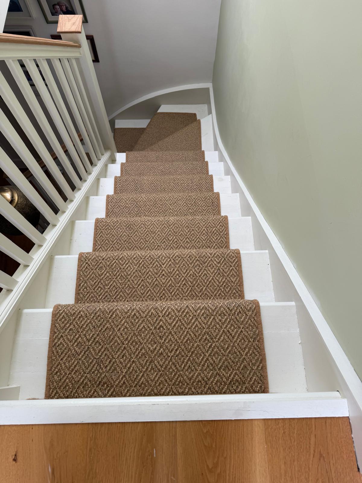 Looking down a white painted staircase dressed with a natural tan sisal-look runner