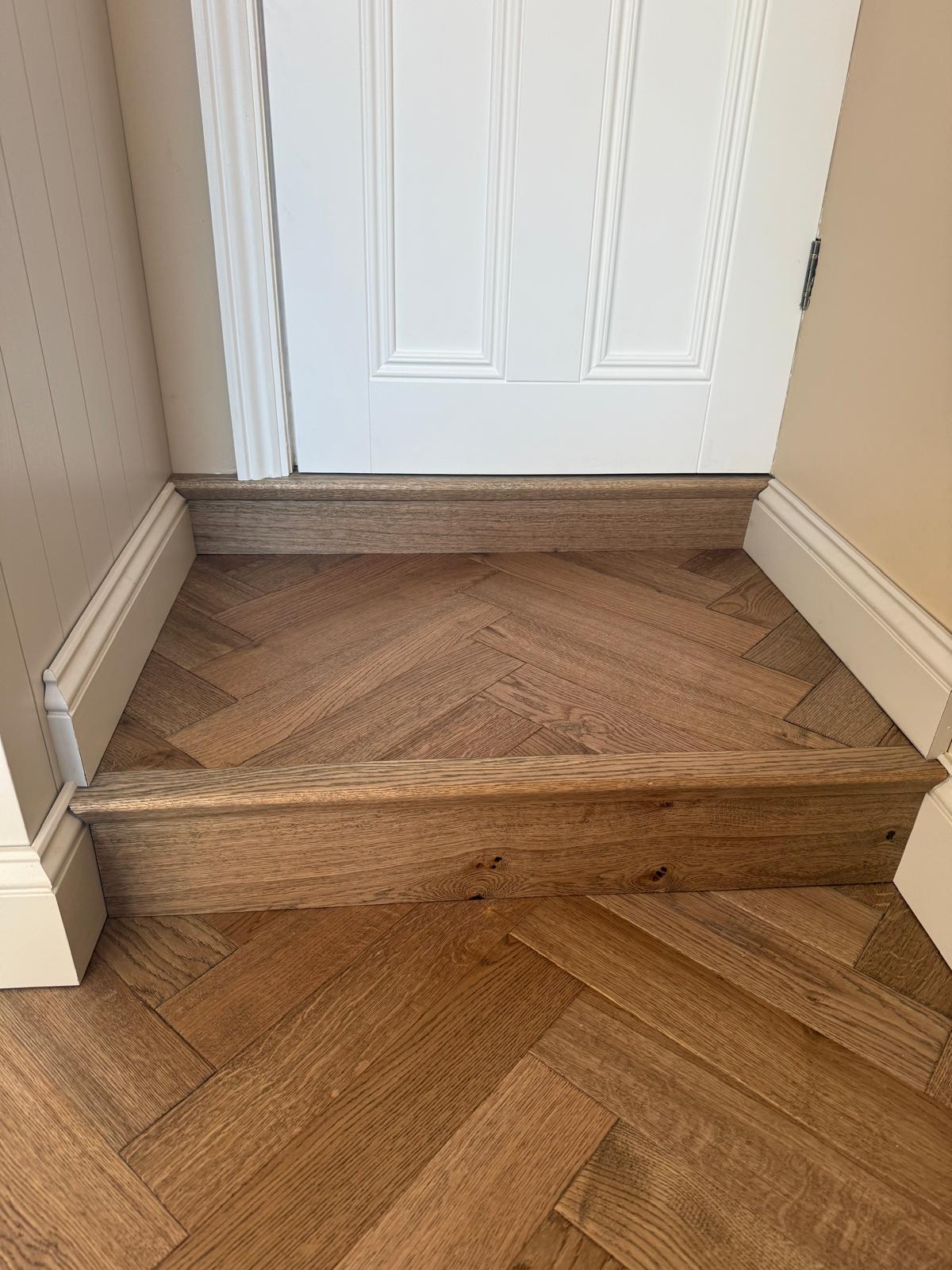 Smoked oak herringbone parquet meeting a white panelled door with a matching timber threshold