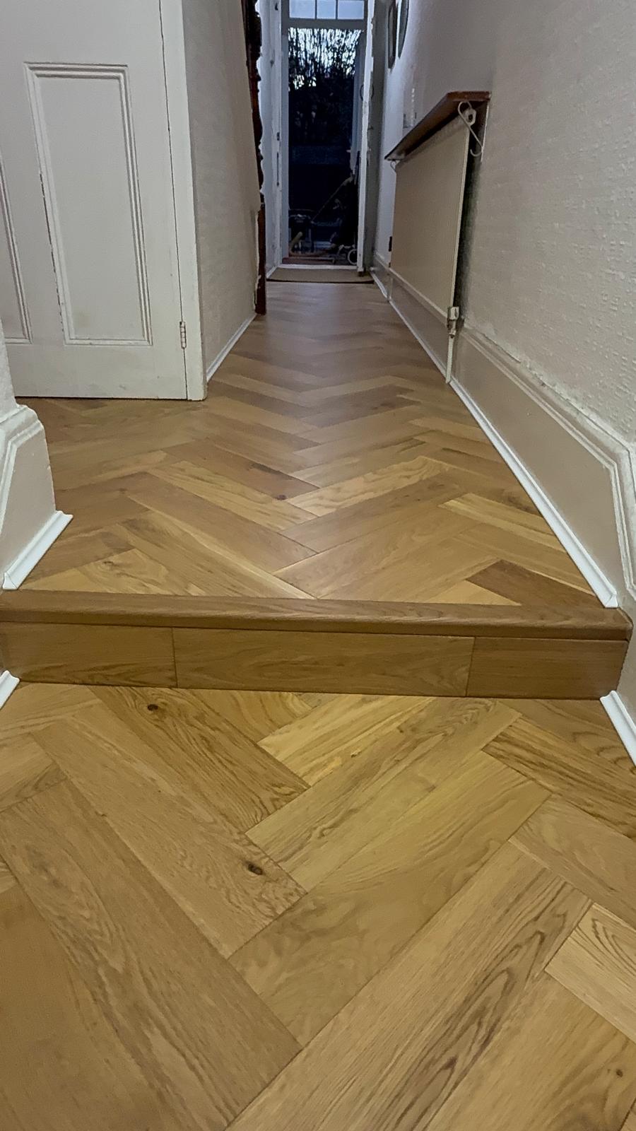 Golden oak herringbone floor running the length of a hallway towards the front door