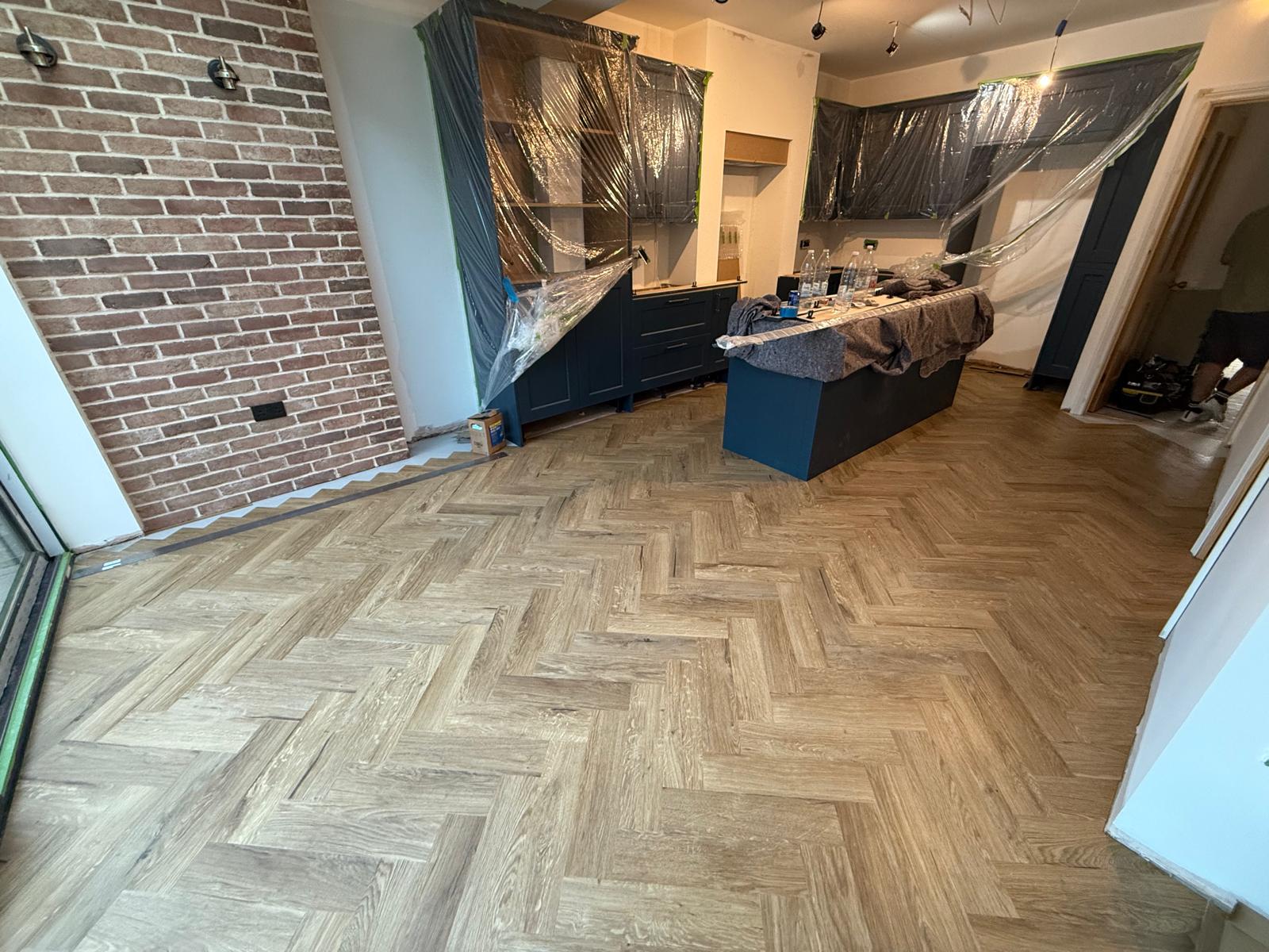 Oak herringbone floor in a kitchen extension beside an exposed brick wall and navy cabinetry