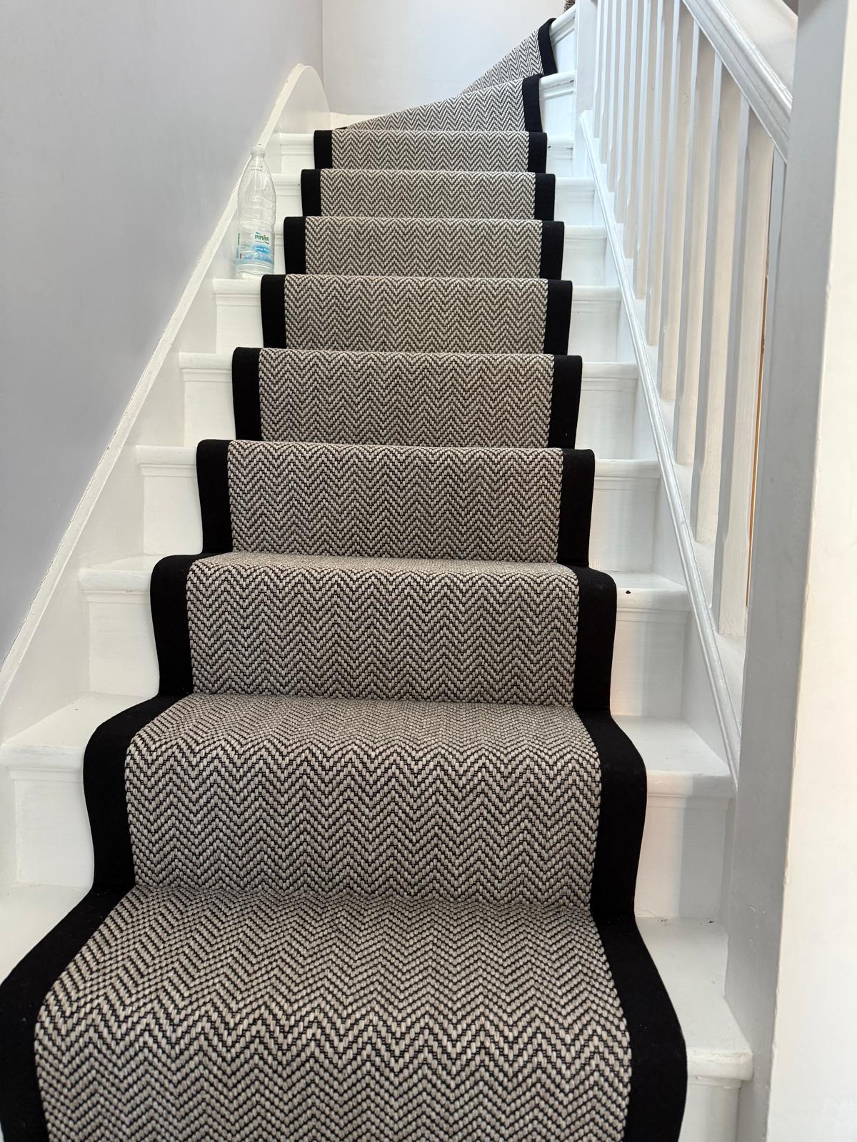 Black and white herringbone stair runner with black binding on white painted stairs