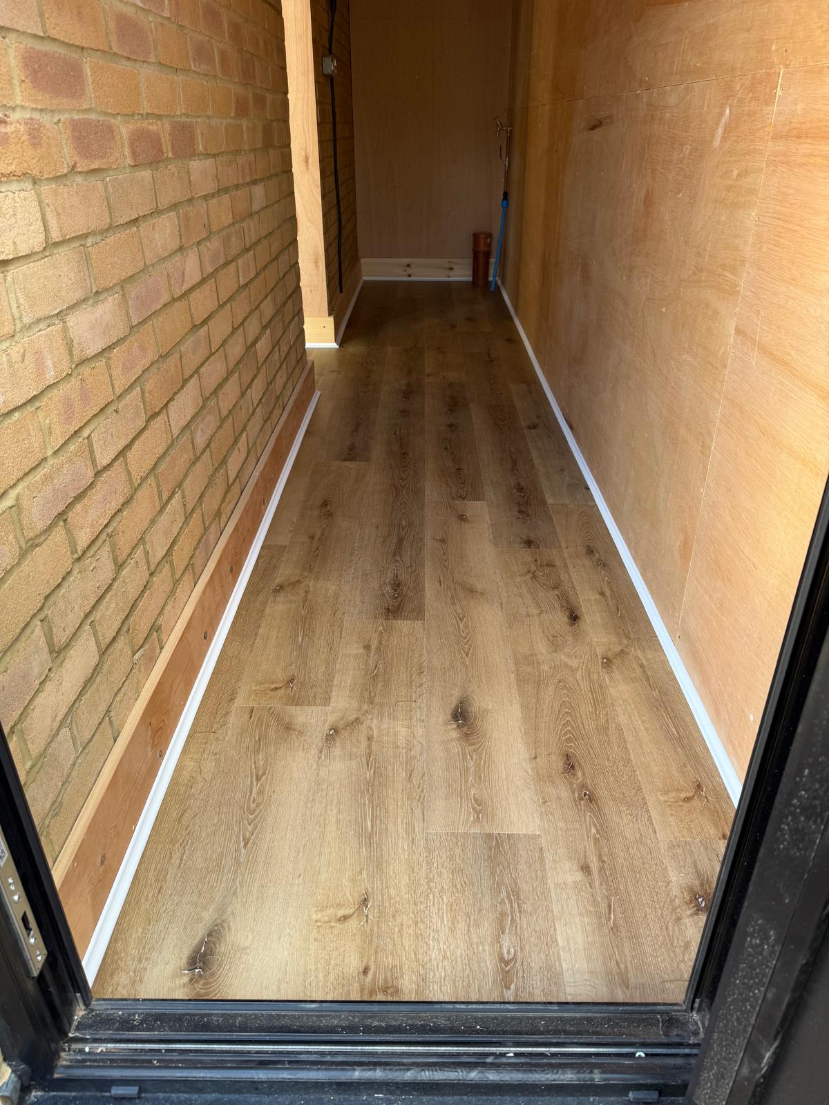 Rustic oak plank floor in a narrow side porch between a brick wall and timber lining